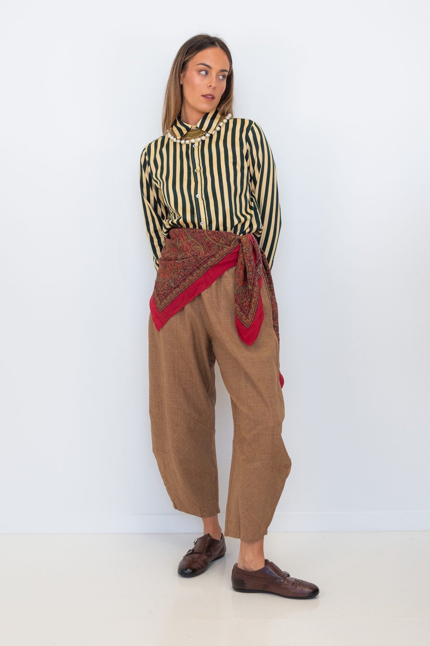 Model wearing Chocolate Prince of Wales barrel pants with a striped shirt and red scarf tied at the waist.
