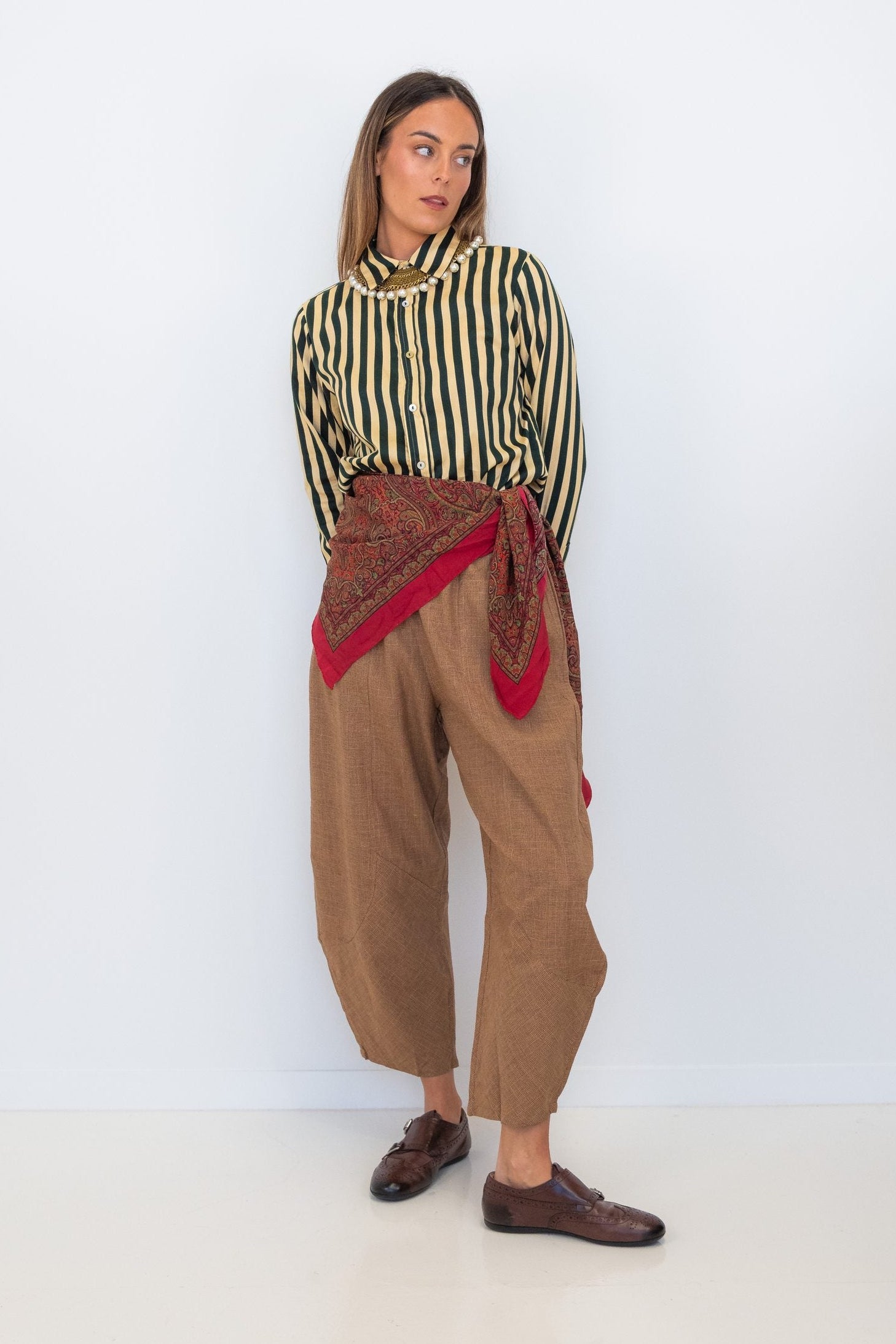 Model wearing Chocolate Prince of Wales barrel pants with a striped shirt and red scarf tied at the waist.
