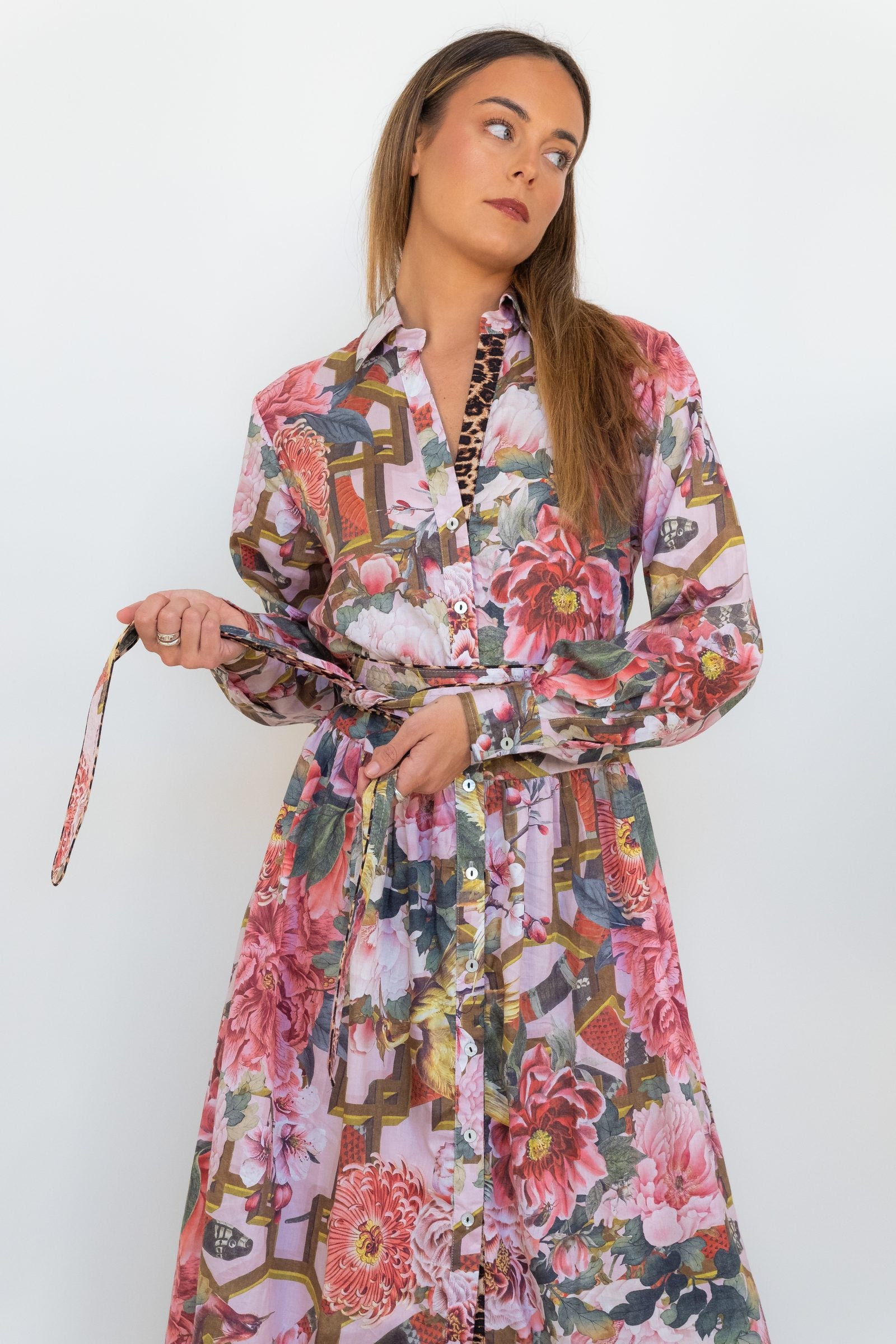 Model adjusting the slim tie belt on the Ophelia pink floral-and-chain print drop-waist dress.