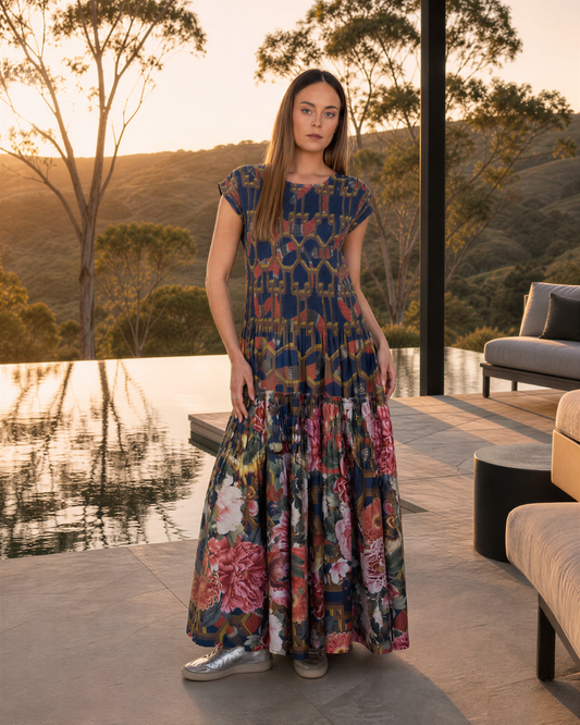 Full-length model wearing the Ophelia snakes and florals smocked maxi dress beside an infinity pool at sunset.