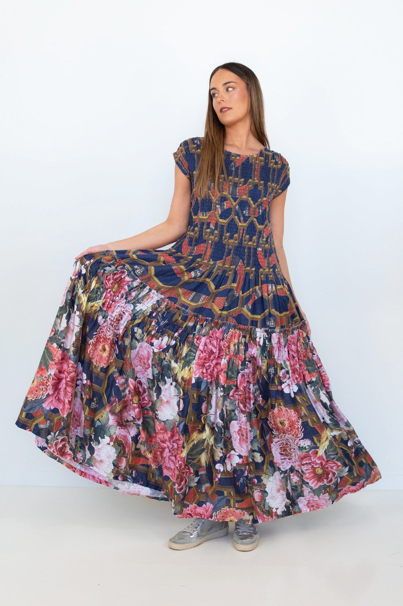 Model holding out the floral tiered skirt of the Ophelia smocked maxi dress to show its volume and movement.