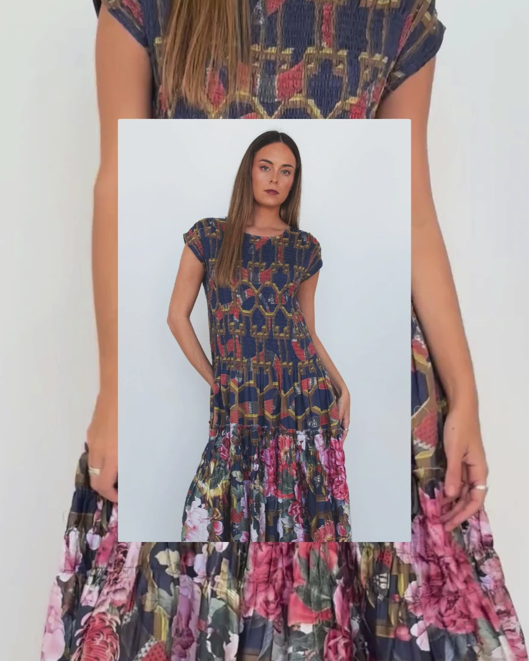 A woman modeling a tiered maxi dress with a navy blue base featuring a gold chain-link pattern on the bodice and a colorful floral print on the skirt.